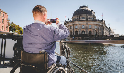 Berlin for everyone, whatever your abilities - Men is sitting in his wheelchari and takes a picture from Berlin and looks for boats