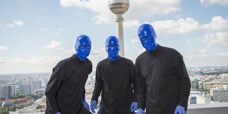 Die BLUE MAN GROUP posiert vor dem Fernsehturm bei strahlend blauem Himmel.
