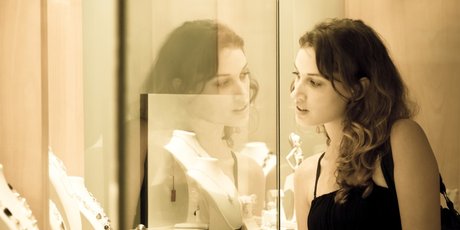Junge Frau schaut in eine Glasvitrine, in der Schmuck ist