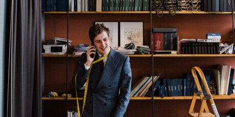 Maximilian Mogg am Telefon, mit einem mit einem Maßband um den Hals in seinem Laden in Berlin.