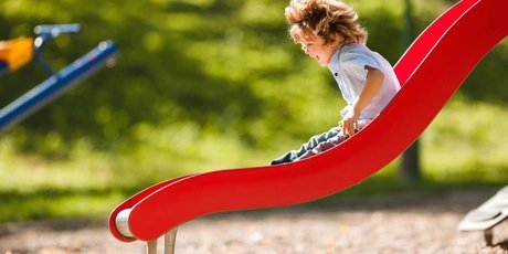 Junge rutscht eine rote Rutsche runter