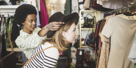 Ladenbesitzerin probiert Hut auf Kundin in Vintage Boutique