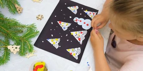 Junges Mädchen bastelt Weihnachtskarte mit Schneemann und Weihnachtsbaum aus Vogelperspektive