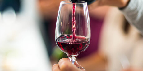 Hand hält Weinglas, während Rotwein eingeschenkt wird 