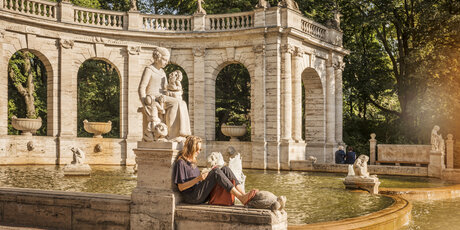 Eine Frau liest am Märchenbrunnen im Volkspark Friedrichshain