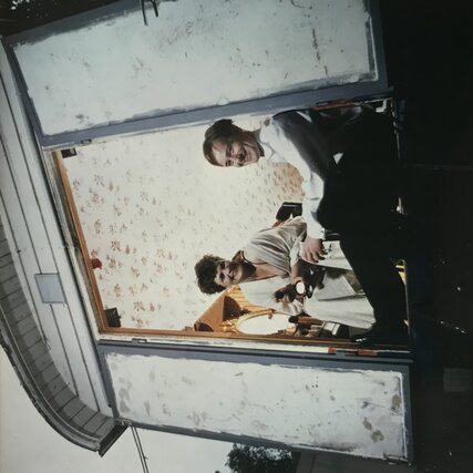 Gayle Tufts und Rainer Bielfeldt lächelnd im Türrahmen eines Bauwagens sitzen.