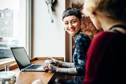 Junge Frau mit Tattoos im Café mit Laptop