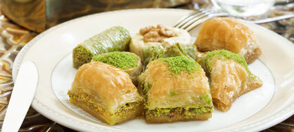 Türkisches Gebäck Baklava aus Blätterteig mit Pistazien und Zuckersirup auf weißem Teller 