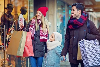Mutter, Vater und Tochter shoppen händchenhaltend Eltern und Kind bummeln am Schaufenster im Winter glücklich und lächeln