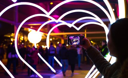 Frau mit Smartphone fotografiert leuchtene Herzformen in der Stadt