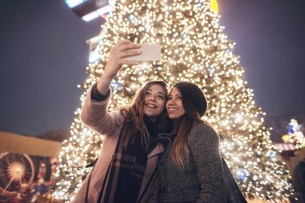 Girlfriends doing selfie in front of christmas tree.