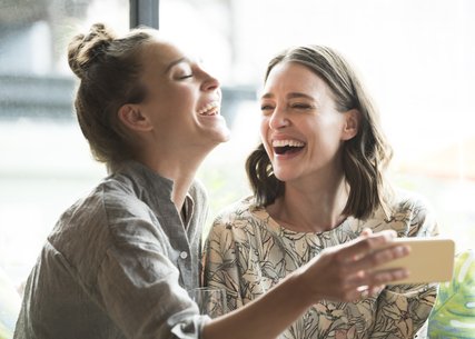 Woman holding mobile phone with freind, laughing