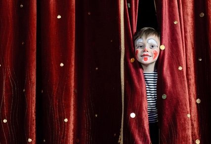 Junge als Clown verkleidet Kind als Clown geschminkt, hinter einem roten Vorhang