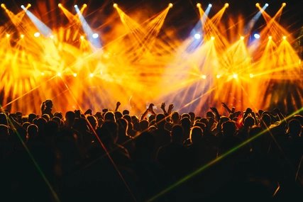 Audience at a concert. Yellow light effects shine above the celebrating crowd.  
