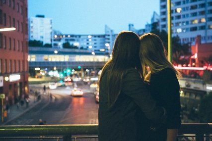 Lesbisches Paar umarmt sich und guckt in Richtung Stadt