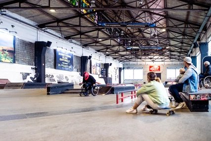 Skatehalle Berlin: Zwei Skater schauen Rollstuhlskater zu