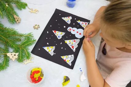 Mädchen dekoriert und schmückt Weihnachtskarte mit Knete Junges Mädchen bastelt Weihnachtskarte mit Schneemann und Weihnachtsbaum aus Vogelperspektive