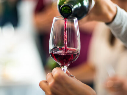 Hand hält Weinglas, während Rotwein eingeschenkt wird 