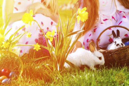 Zwei Mädchen auf der Wiese an Ostern mit einem Korb, Kaninchen und Osterglocken