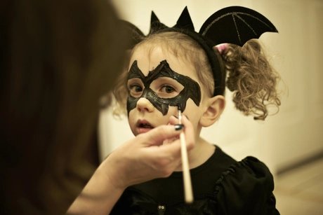 Mother painting daughters face for halloween bat costume