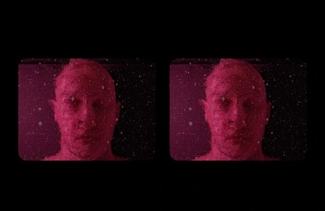 Video still: Frontalansicht einer Person mit geschlossenen Augen in einer Art Flüssigkeit. Das Still zeigt die selbe Ansicht zweimal nebeneinander und pink eingefärbt. Um beide Fenster herum liegt ein schwarzer Rahmen.