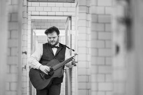 Svavar Knútur mit Gitarre zwischen einem Türrahmen nachdenklich nach unten schauend.