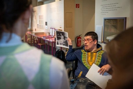 Mann in Ausstellung zeigt einer Gruppe ein historisches schwarz-weiß-Foto von Anne Frank.