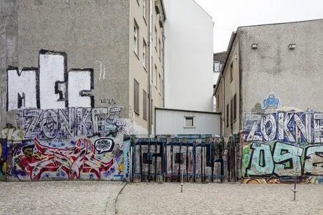 Zwei Häuser und zwischen ihnen ein Zaun. Alles ist mit bunten Graffiti bedeckt.
