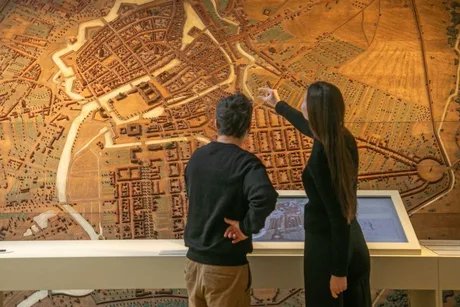 Besucherin und Besucher vor einem Stadtmodell mit Medienstation
