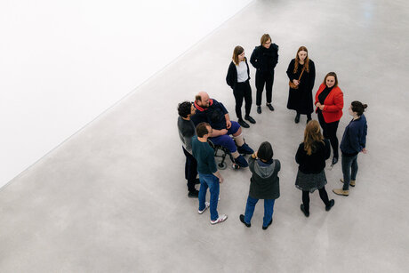 Eine Gruppe von Personen steht im Kreis in einem großen Raum und unterhält sich.