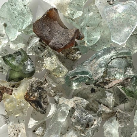 Zerbrochene Glasscherben in verschiedenen Formen und Farben, darunter grün, braun und klar, mit rauen und glatten Oberflächen.