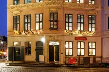 Nacht-Ansicht der stuckverzierte Außenfassade mit hell erleuchteten Fenstern, leuchtendem Weihnachtsschmuck und geöffneter Eingangstür.