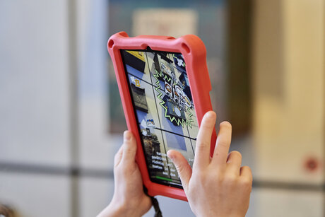 Zwei Hände halten ein Tablet hoch in die Luft, auf dem eine Augmented Reality Anwendung zu sehen ist.