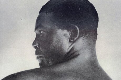 Die alte Schwarz-Weiß Aufnahme zeigt den Autor und Schauspieler Louis Brody von hinten im Büstenporträt: Er blickt über seine linke, nackte Schulter, so dass sich sein Profil mit einem festen Blick gegen einen hellen Hintergrund abzeichnet.