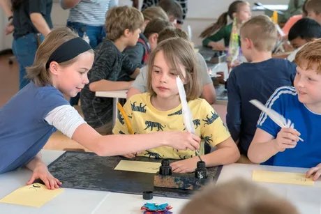 Kinder im Museumslabor schreiben mit Tinte und Feder