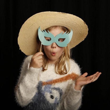 Ein mit Sonnenhut verkleidetes Kind hält sich eine Stab-Papiermaske vor die Augen und formt mit den Lippen ein O