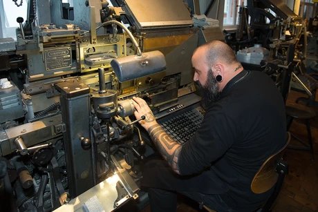 Ein Mann arbeitet an einer großen, schwarzen Setzmaschine.