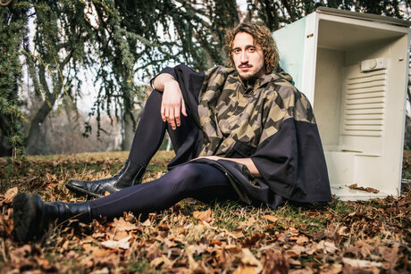 Berni Wagner draußen in Laub an einem alten Kühlschrank sitzend angelehnt.
