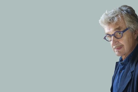 Ein Mann mit grauen Haaren und blauer Brille schaut schmunzelnd aus dem rechten Bildrand in die Kamera.