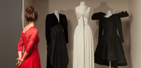 Eine Person, von hinten, im roten Kleid betrachtet Kleider in der Modegalerie des Kunstgewerbemuseums