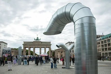 Zwei große, gebogene Metallstrukturen stehen auf dem Pariser Platz vor dem Brandenburger Tor. Menschen versammeln sich in der Nähe.