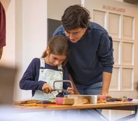 Mann und Kind beim gemeinsamen Sägen für ein Musikinstrument im Museumslabor
