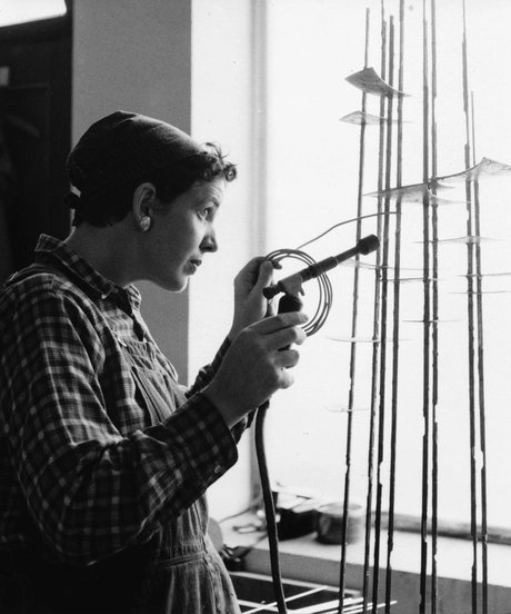 Schwarz-weiß-Foto, das die Künstlerin im Seitenprofil zeigt, während sie mit einem Lötkolben an einer Skulptur arbeitet.