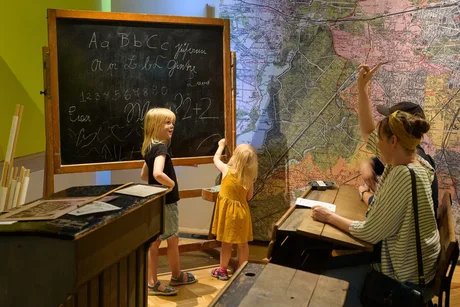 In der Ausstellung BerlinZEIT spüren Eltern mit Kindern umgeben von historischem Mobiliar den Schulalltag der Kaiserzeit nach.