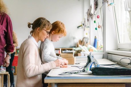 Eine erwachsene Person und ein Kind sitzen an einem Werktisch im Atelier Bunter Jakob und toben sich kreativ aus.
