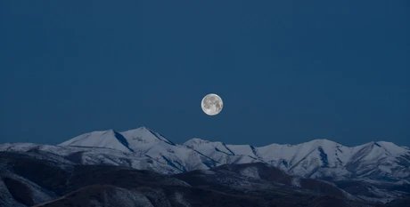 Der Mond knapp über einem Bergkamm am Horizont.
