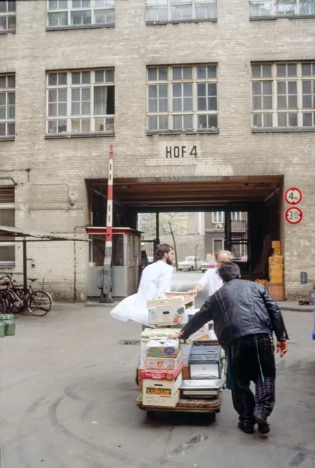 Drei Männer schieben eine mit Kisten beladene Karre durch einen Hinterhof