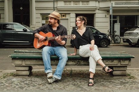 Anne Helm und Marcel Weller mit Gitarre sitzen auf einer Bank.