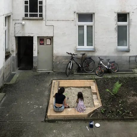 Frau mit Kind im Sandkasten eines Berliner Hinterhofs