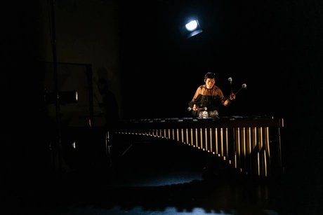Eine Musikerin spielt mit Schlegeln auf einem Marimbaphon, beleuchtet von einem einzelnen Scheinwerfer.